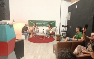 Las 3 ponentes sentadas con algo de publico a la derecha, en el turno de respuestas.